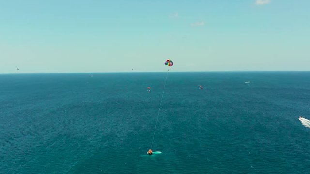 People flying on a colorful parachute towed by a motor boat, aerial view. Parasailing in blue sky.