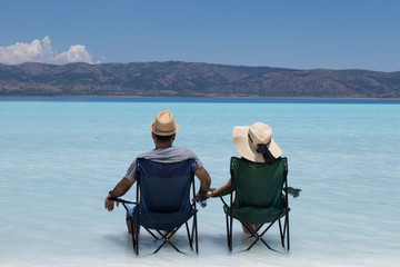 the beautiful girl and handsome man wearing wicker hats and sitting camp chairs in the lake and looking at the Salda lake from Turkey.