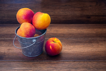 Peaches in a bucket over wooden background with copy space 