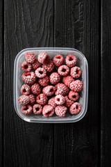 Freezing berries. Frozen raspberries in container on black background