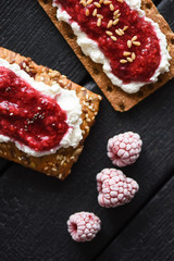 Healthy dessert flat lay. Chia seed jam with creamcheese, flax seeds and raspberries on wholegrain crispbread on black background