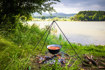 Cooking outdoor on a fire in a pot. Preparing  goulash in a nature by the lake.