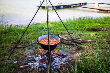 Cooking outdoor on a fire in a pot. Preparing  goulash in a nature by the lake.