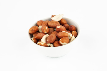 Pile of raw unpeeled peanut in white ceramic bowl on white background