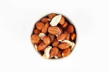 Pile of raw unpeeled peanut in white ceramic bowl on white background, top view