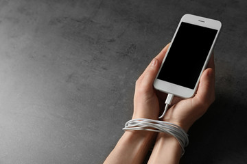 Woman holding mobile phone in hands tied with charging cable on grey background, closeup....