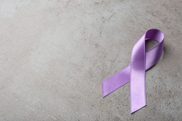 Purple ribbon on grey stone background, space for text. Domestic violence awareness