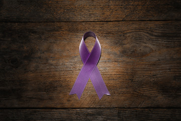Purple ribbon on brown wooden background, top view. Domestic violence awareness