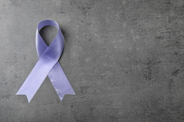 Purple ribbon on grey stone background, top view with space for text. Domestic violence awareness