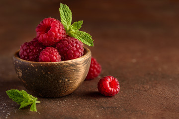 Fresh raspberry berries close-up in a wooden bowl on a brown background. Selective focus