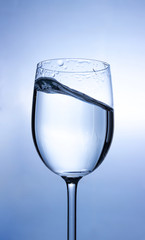 Transparent liquid (water) splash micro wave inside the wine glass on a white background