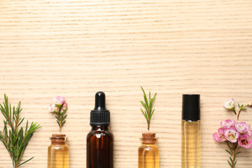 Flat lay composition with bottles of natural tea tree oil and space for text on wooden background