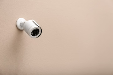 Modern CCTV security camera on beige wall. Space for text