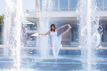 young woman performing a yoga pose in city fountain