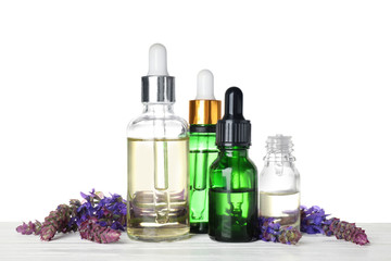 Bottles of sage essential oil and flowers on wooden table, white background