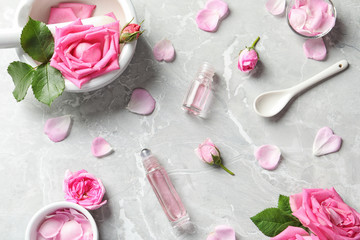 Flat lay composition with rose essential oil and fresh flowers on grey table