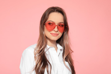 Fototapeta premium Portrait of beautiful young woman with heart shaped sunglasses on color background