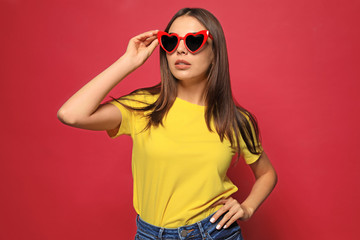 Naklejka premium Portrait of beautiful young woman with heart shaped sunglasses on color background