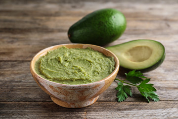 Bowl with guacamole and ripe avocados served on brown wooden table