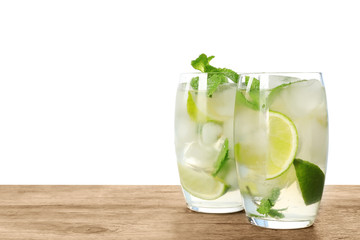 Glasses of refreshing drink with lime slices and mint on wooden table against white background