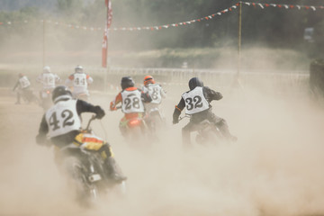 Racing motorcycles making a lot of dust when accelerating after the turn on the dirt racing track.