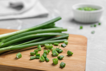 Wooden board with bunch of fresh green onion on table, closeup