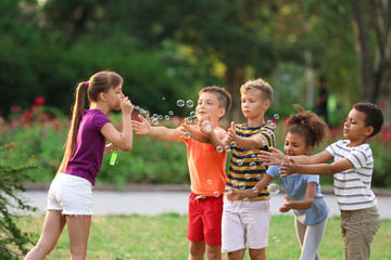 Fototapeta premium Cute little children playing with soap bubbles in park