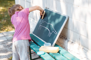 A girl drawing a cat on the blackboard outside. 