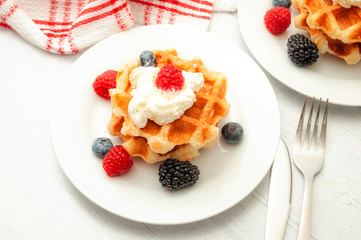Wholesome breakfast, healthy dessert and waffle snack concept theme with a  plate of belgian waffles with blueberries, blackberries, raspberries and whipped cream on a rustic white wooden table