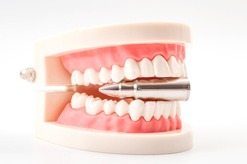 Obraz premium Bite the bullet, stoic attitude or endure an unavoidable painful or unpleasant situation concept theme with teeth biting on a silver bullet isolated on white background