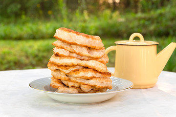 Traditional Bulgarian (Balkan) homemade breakfast Mekitsi (Mekici). Fried dough in deep oil on white table with green leaves background
