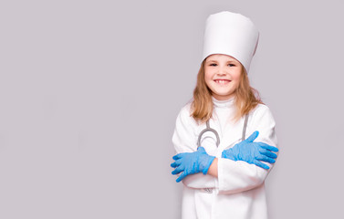 Smiling little girl in medical uniform and blue gloves looking at camera isolated on white