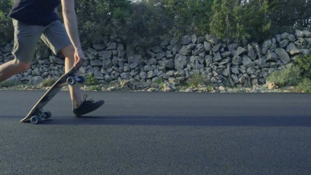 Slow motion video of an unrecognizable young skateboarder jumping on a skateboard. Still shot, actor moving from left to right.