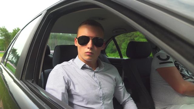 a young guy, a man in sunglasses, sits in the car and opens the window, lowers the side window.