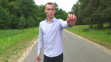 A young guy walks on the road, turns, waves his hand, shows his palm and goes on. goodbye - Powered by Adobe
