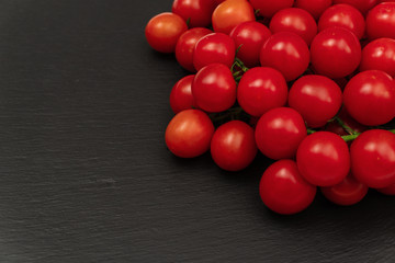 A branch of red cherry tomatoes on a dark slate background. Small and juicy vegetable is rich in vitamins and trace elements. Healthy food. Fresh and organic vegetables. Raw food