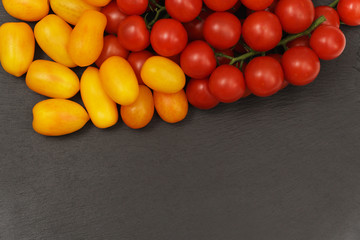Scattered red and yellow tomatoes on the dark surface of the slate. Small and juicy vegetable is rich in vitamins and trace elements. Healthy food. Fresh and organic vegetables. Raw food