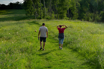 Couple hiking on trail with small dog at sunset in a grassland prairie with trailing shadows