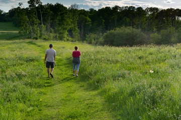 Fototapeta na wymiar Couple hiking on trail with small dog at sunset in a grassland prairie with trailing shadows