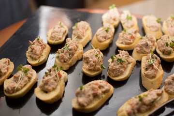 Gourmet appetizer concept. Party chicken or Tuna appetizer on a black table. Slices of baguette with fresh tuna or chicken with vegetables on top. Christmas meal concept.