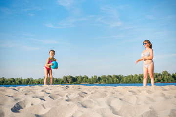 Mother and daughter playing with a blue ball on the river bank. A healthy way of life.