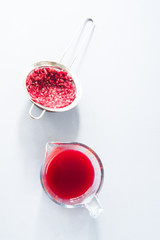 Pomegranate juice, colander with carcasse of pomegranate seeds over a gray background