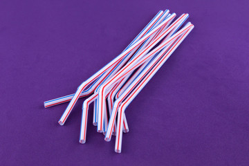 Plastic utensils cocktail tubes on a purple background close-up