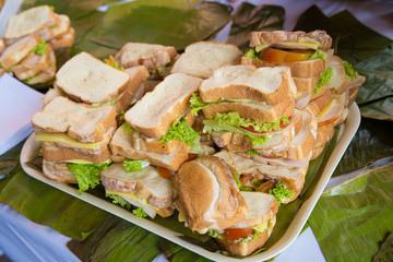 Bunch of sandwiches on a table full of platano leafs. Sandwich with ham, lettuce, cheese, tomatoes and white bread. Children snack concept.