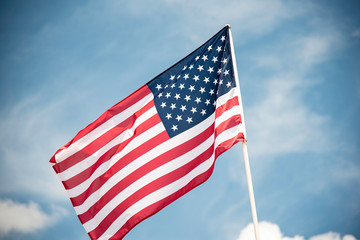 An American flag fluttering in the wind against a blue sky with clouds.