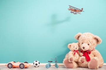 Retro Teddy Bears, old toy trike bicycle, obsolete plastic car, soccer ball, flying wooden plane front aquamarine wall background. Mother or father with baby concept. Vintage style filtered photo
