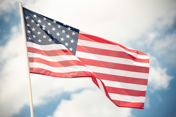 An American flag fluttering in the wind against a blue sky with clouds.
