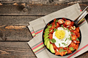 mexican breakfast Chilaquiles . tortilla chips are lightly stewed in a red tomato and paprika chili sauce, scrambled eggs are added and served in a pan with avocado and green onions and cilantro. 