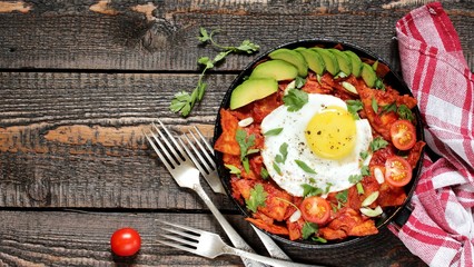 mexican breakfast Chilaquiles . tortilla chips are lightly stewed in a red tomato and paprika chili sauce, scrambled eggs are added and served in a pan with avocado and green onions and cilantro. 