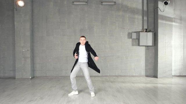 Trendy caucasian boy performing dance moves in studio. Young stylish man performing contemporary dance on grey background.